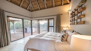 Ein Schlafzimmer mit einem großen Bett, einem Deckenventilator und Blick ins Freie durch eine Glastür.