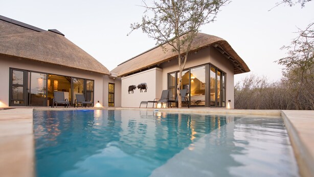 Ein modernes Haus mit Swimmingpool, großen Fenstern und einem Strohdach.