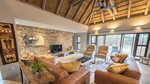 Ein großzügiges Wohnzimmer mit Steinwand, Ledersofas, einem Holztisch und einem Flachbildfernseher.