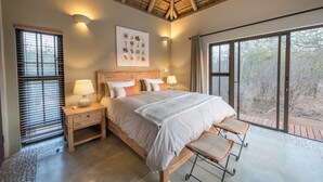 Ein Schlafzimmer mit einem großen Bett, Nachttischen aus Holz, einer Bank, einem Deckenventilator und Blick ins Freie.