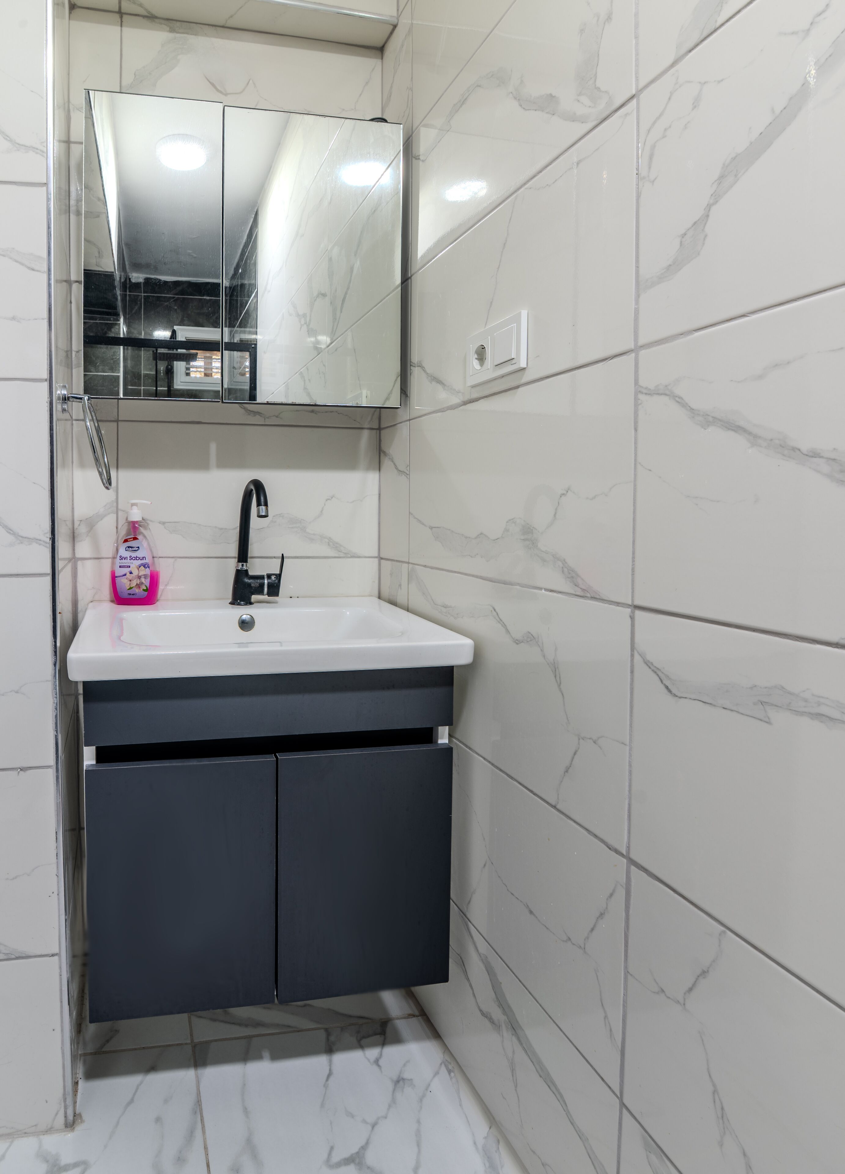 A bathroom with a white sink, dark cabinets, and a mirror above the sink.