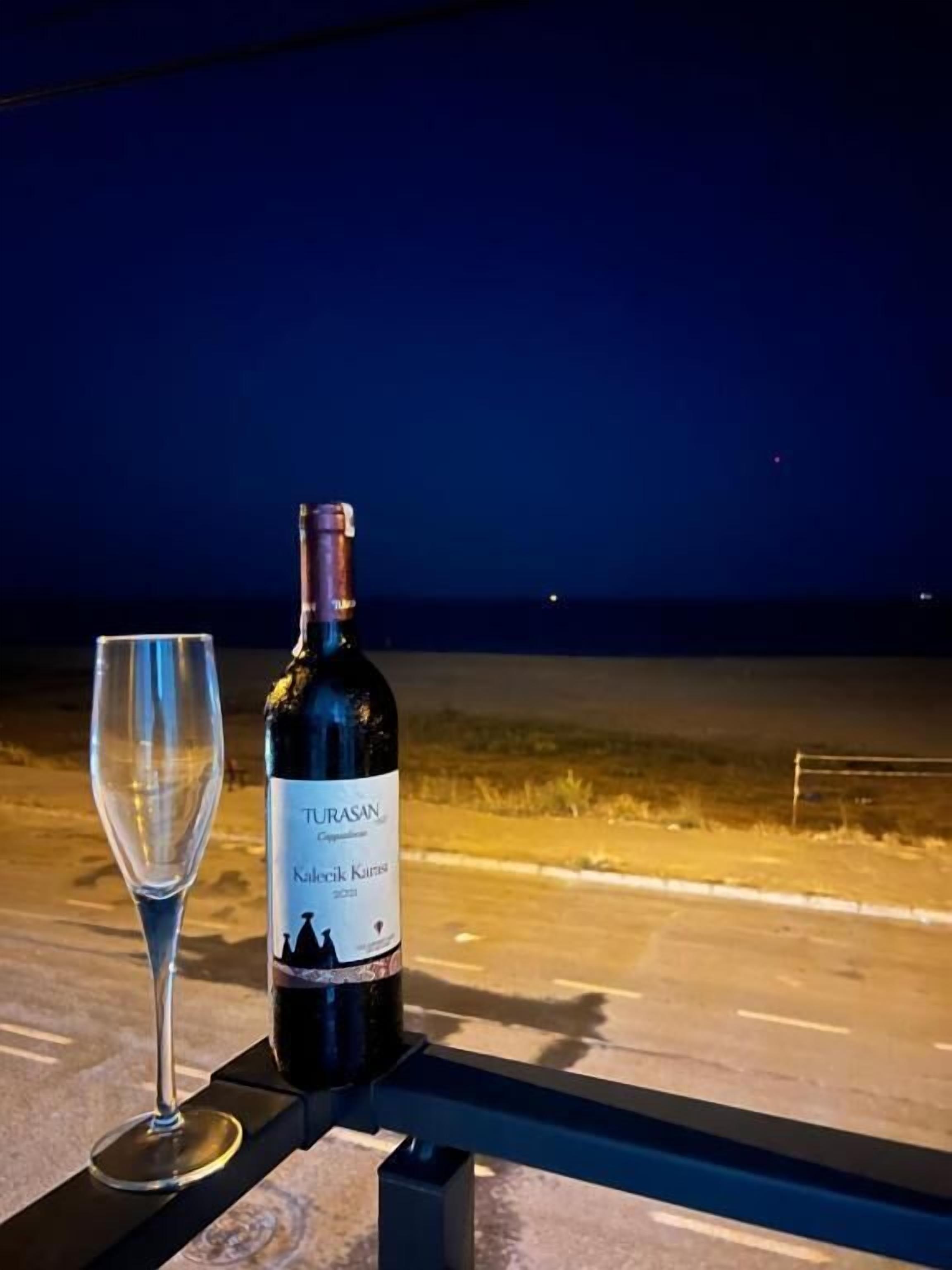 Une bouteille de vin Turasan et un verre vide sur une table à l’extérieur, la nuit.