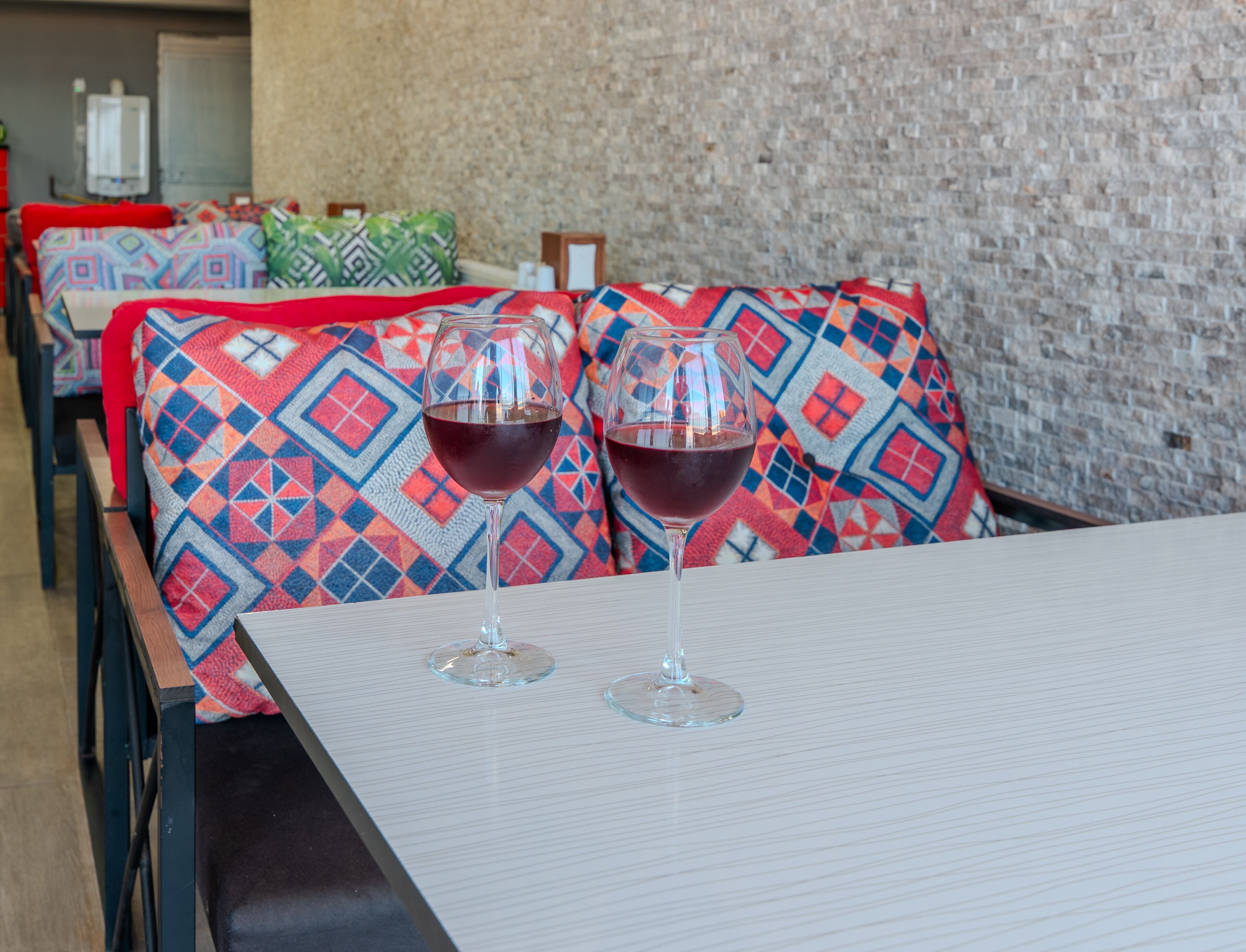 A dining area with a table set for two, featuring two wine glasses. The seating includes colorful patterned cushions.