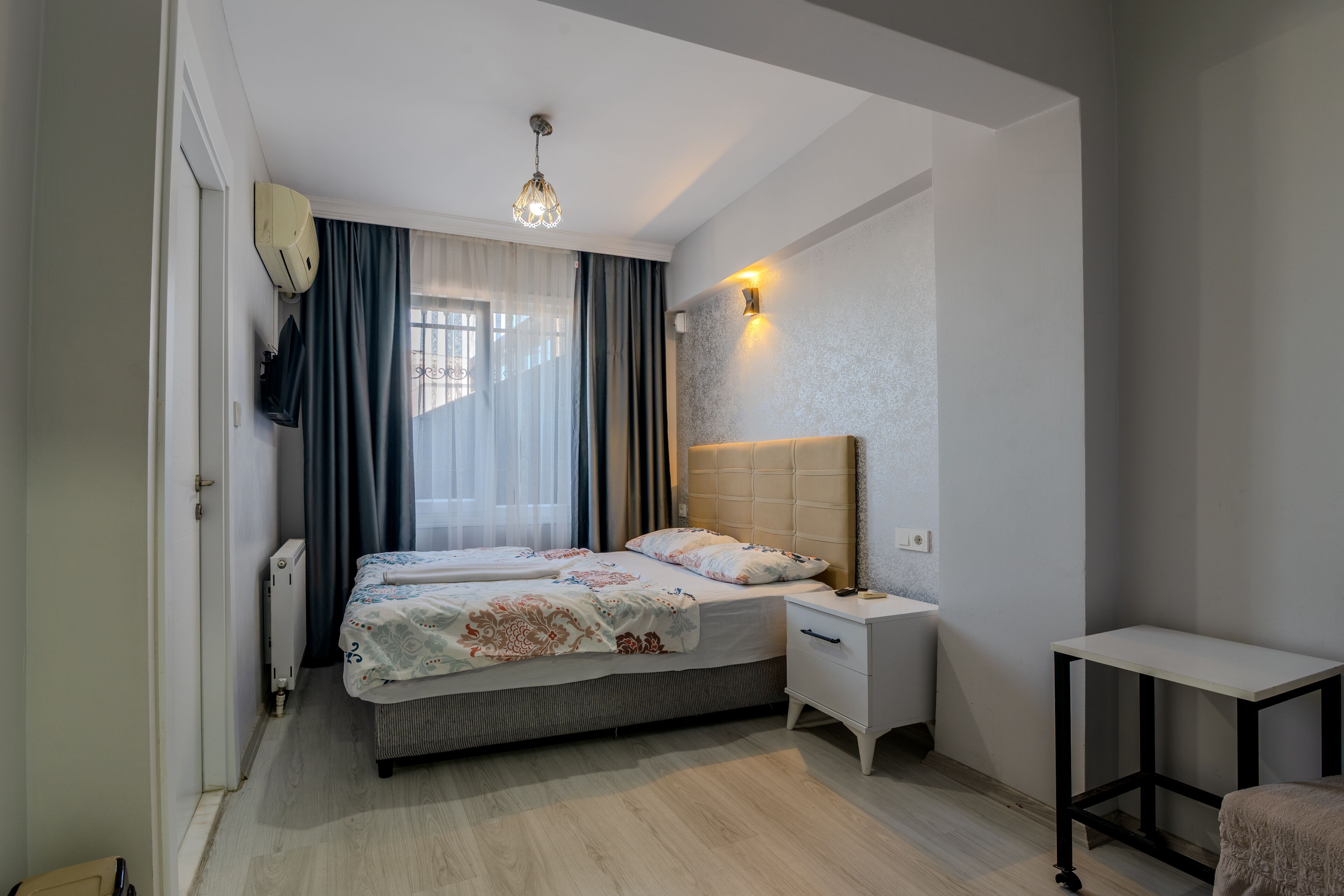 A bedroom with a bed, bedside tables, a nightstand, a small table, and a ceiling light.