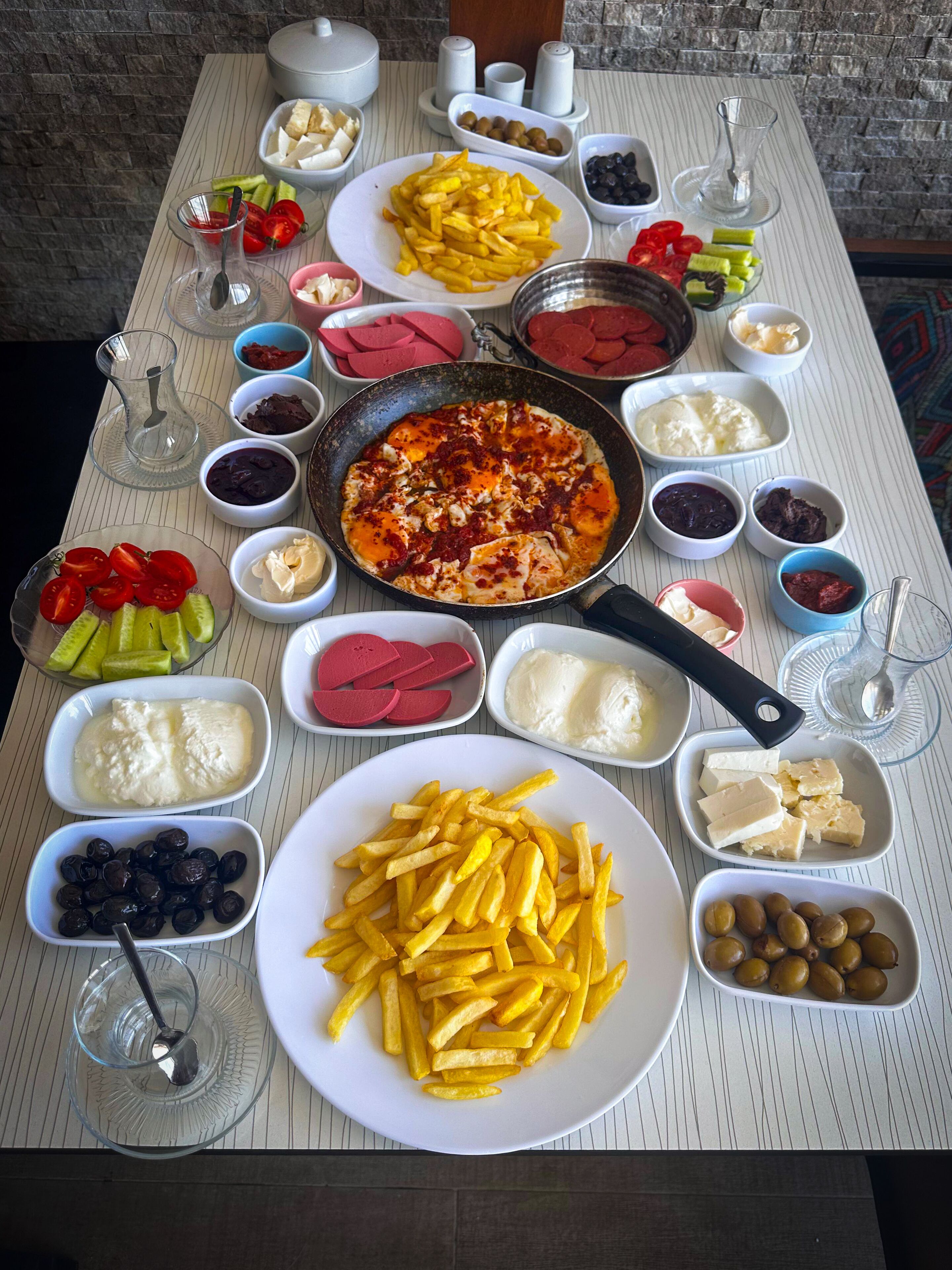 Een tafel met diverse etenswaren, zoals frieten, olijven en een schaal met eten.
