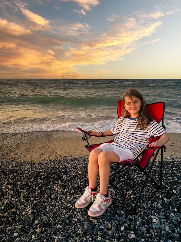 A person sitting on a beach chair facing the ocean with waves.