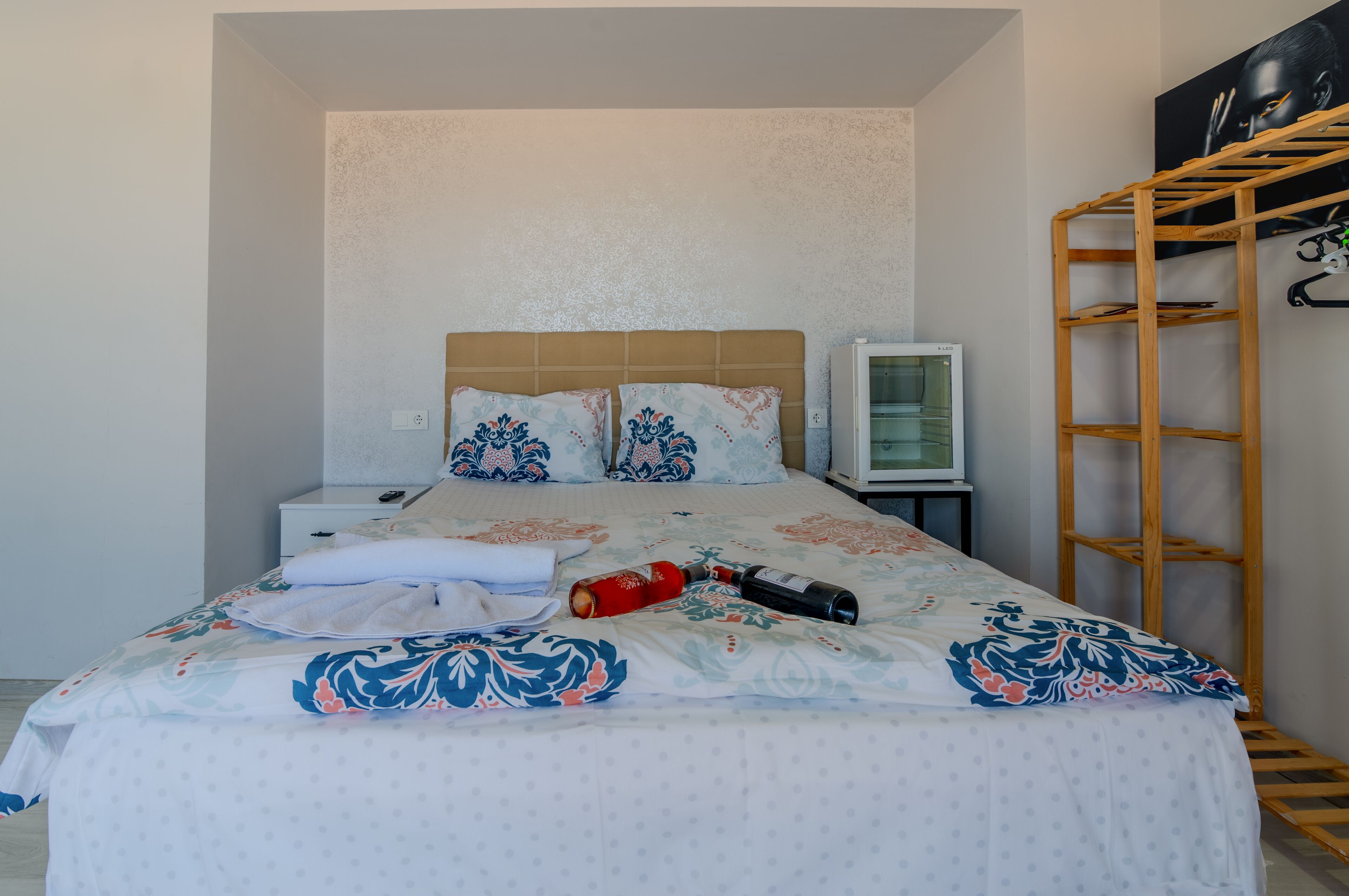A bedroom with a bed, a television, a wooden shelf, and a wall-mounted artwork.