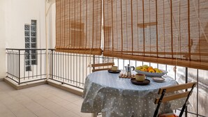 Un balcón con una mesa dispuesta para dos personas, con un mantel de lunares, una jarra de metal y un cuenco de fruta.