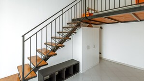 Una escalera moderna con escalones de madera y barandillas metálicas, que conduce a una habitación con paredes blancas y un armario empotrado.