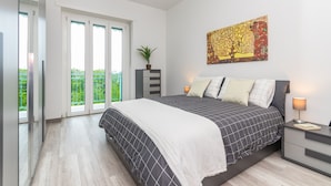 A bedroom with a large bed, a nightstand, a lamp, a painting, a plant, and a sliding door leading to a balcony. - Il Rifugio del Viaggiatore by Wonderful Italy (Torino)