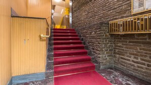A staircase with red carpet leading to a room with a wooden door and a stone wall. - Il Rifugio del Viaggiatore by Wonderful Italy (Torino)