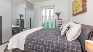 A bedroom with a large bed, a mirror, a window with a view of buildings, and a painting on the wall. - Il Rifugio del Viaggiatore by Wonderful Italy (Torino)