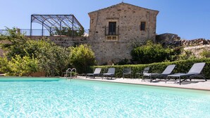 A swimming pool with lounge chairs, a stone building, and a metal structure in the background. - Dependance a Baglio il Corvo by Wonderful Italy (Gangi)