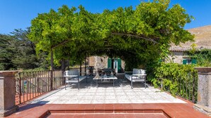 A terrace with outdoor seating, a stone wall, and a view of a building with green shutters. - Dependance a Baglio il Corvo by Wonderful Italy (Gangi)
