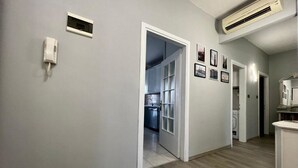 Un couloir avec une porte donnant sur une cuisine, un téléphone fixé au mur et un appareil de climatisation.