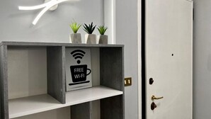 Une chambre moderne au design minimaliste, avec une porte blanche, une étagère portant un panneau indiquant que le Wi-Fi est gratuit, et trois petites plantes en pot.