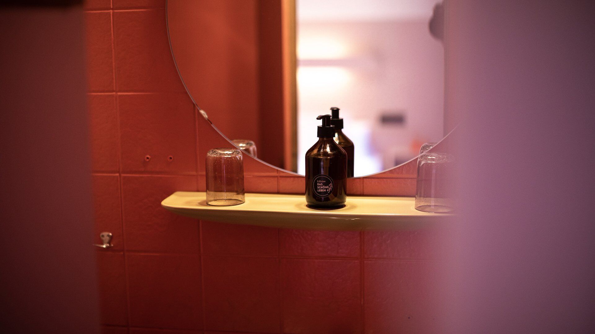 Un baño con un espejo, una botella de jabón líquido y un vaso.