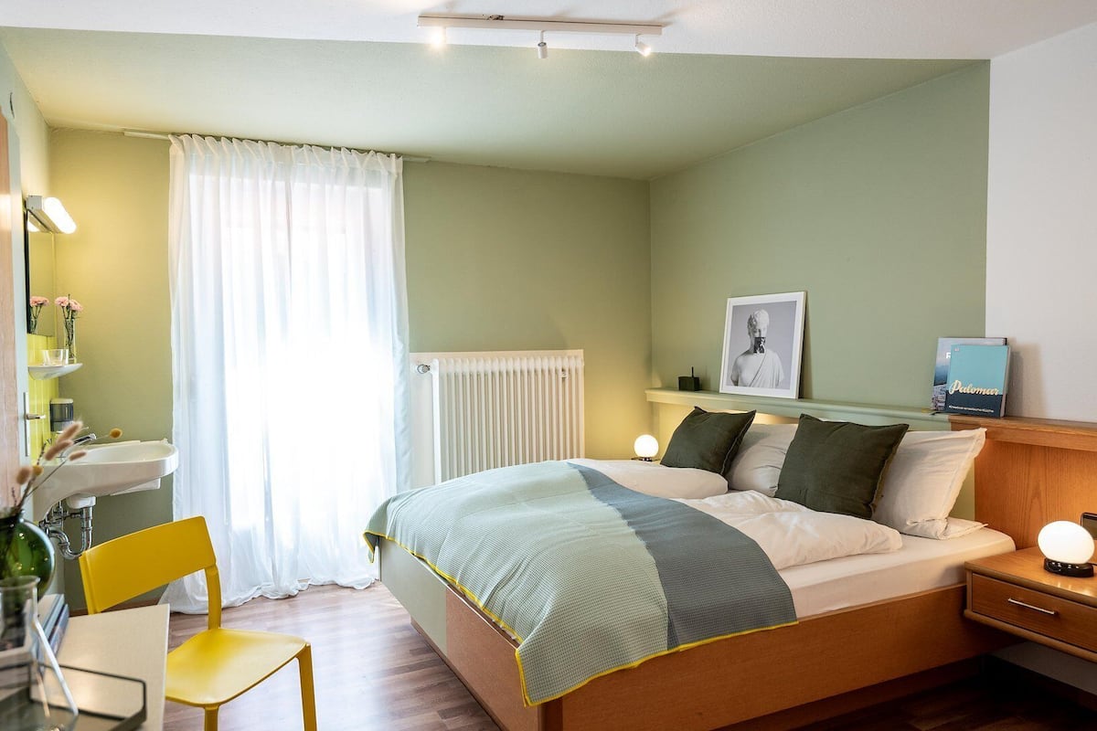 Une chambre à coucher avec un lit, une table de chevet, une lampe et une fenêtre avec des rideaux.