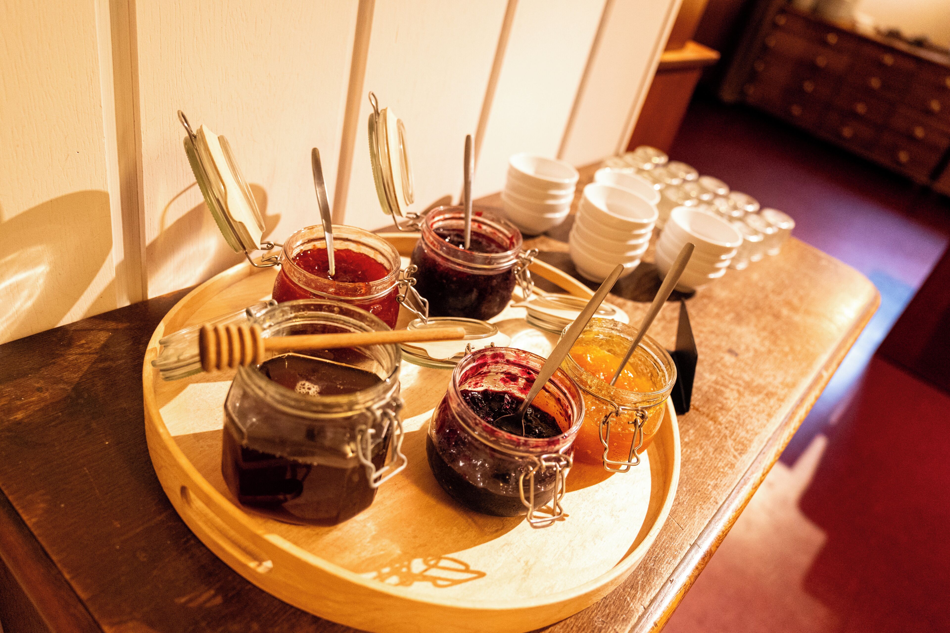 Een dienblad met potten jam en honing, met een honinglepel en lepel, op een houten tafel.