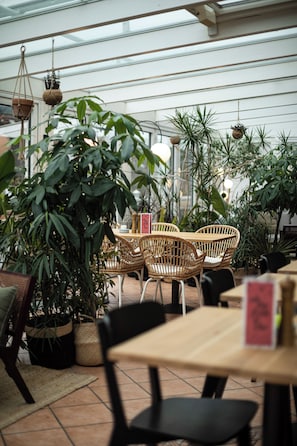 An indoor dining area with wicker chairs, a wooden table, and various potted plants.