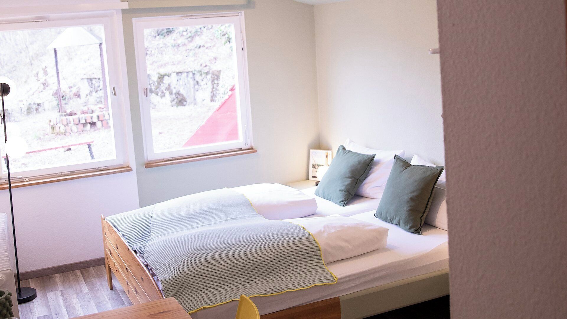 A bedroom with a bed, a bedside table, a lamp, and a window with a view of a red structure.