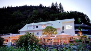 A modern building with a white exterior, a covered outdoor seating area, and a view of a forested hillside. - DAS SCHÖNE LEBEN Pop-Up Hotel (Hornberg)