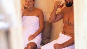 Two people in a sauna, one with a towel wrapped around their body, seated on a bench. - DAS SCHÖNE LEBEN Pop-Up Hotel (Hornberg)
