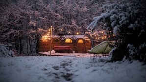 A rustic wooden building with a bench and string lights, surrounded by snow-covered trees. - DAS SCHÖNE LEBEN Pop-Up Hotel (Hornberg)