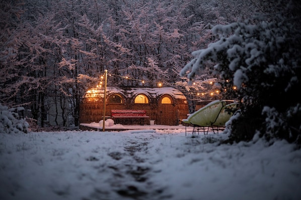 Ein rustikales Holzgebäude mit einer Bank und Lichterketten, umgeben von schneebedeckten Bäumen.