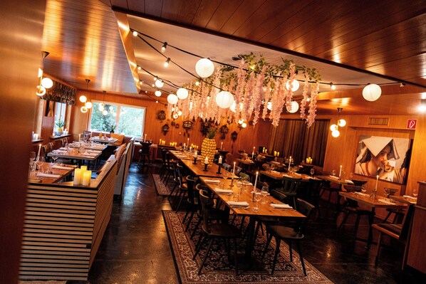A restaurant with wooden interiors, string lights, hanging floral decorations, and tables set for dining.