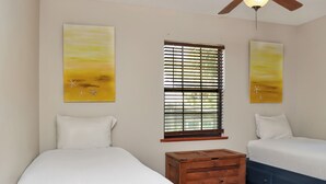 Ein Schlafzimmer mit zwei Betten, hölzernen Nachttischen, einem Deckenventilator und Bildern an den Wänden.