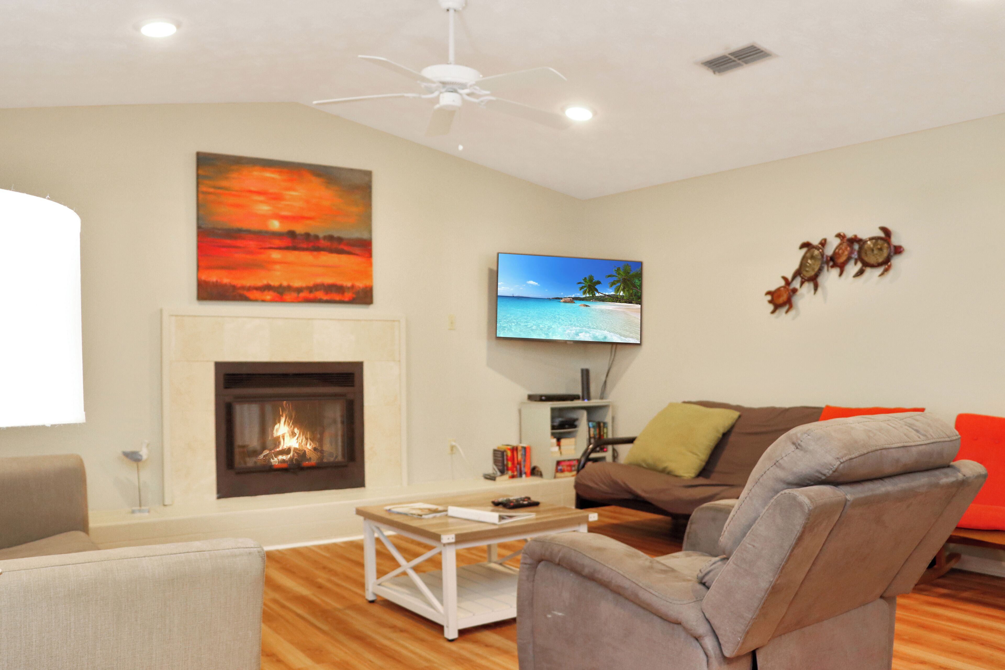 Una sala de estar con chimenea, ventilador de techo, televisor de pantalla plana y un sofá con cojines naranjas.