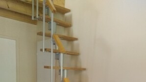 Una escalera de madera con barandillas metálicas que conduce a una plataforma con microondas y una mesita.