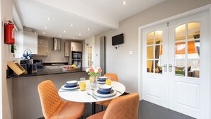 A modern kitchen with a dining area, featuring a round table with orange chairs, a white ceiling, and a fire extinguisher on the wall. - Avenue House (Heald Green, Cheadle) (Heald Green)
