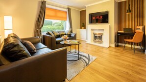A modern living room with a sofa, coffee table, fireplace, and a TV mounted on the wall. - Avenue House (Heald Green, Cheadle) (Heald Green)