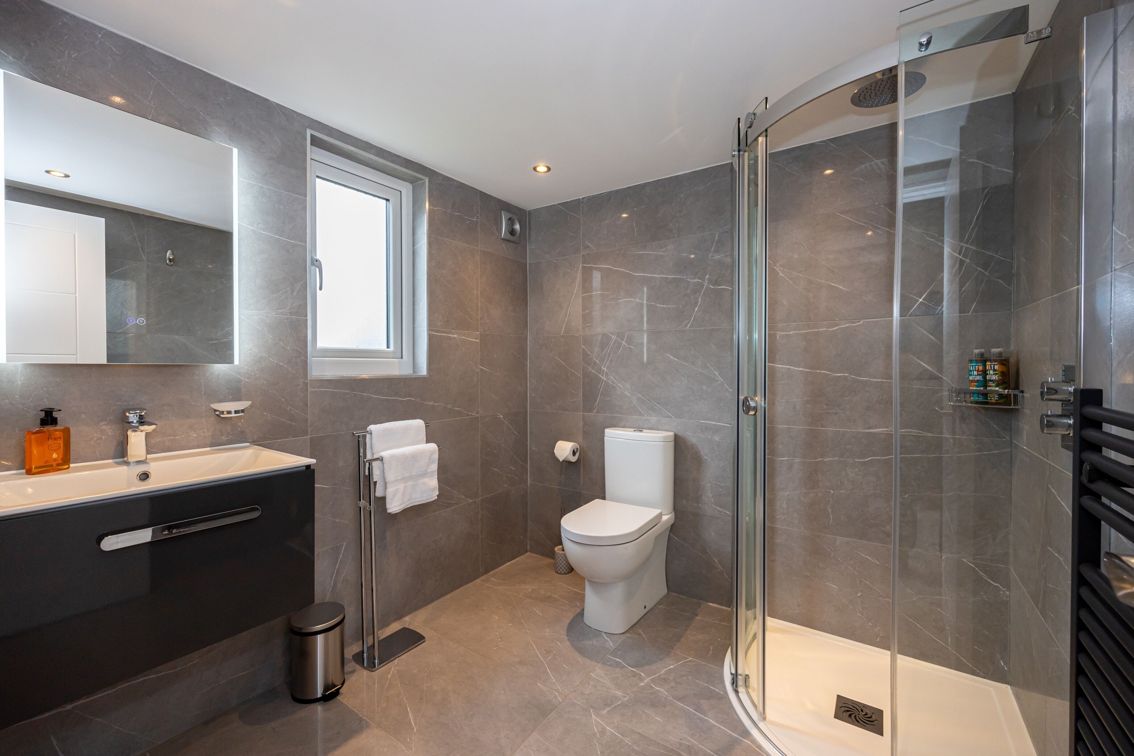 Een moderne badkamer met een glazen douchecabine, een grote spiegel, een donkere wastafel en een toilet.