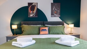 A neatly made bed with green bedding and two white towels, a pillow labeled "Prime Mode," and two wall-mounted lamps on either side. - Avenue House (Heald Green, Cheadle) (Heald Green)