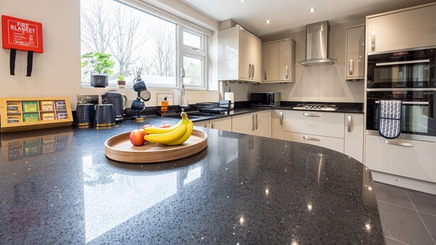 A modern kitchen with a granite countertop, stainless steel appliances, and a window with a view of trees. - Avenue House (Heald Green, Cheadle) (Heald Green)