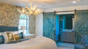 Un dormitorio con una cama grande, una araña y vistas a un baño a través de una puerta de madera.