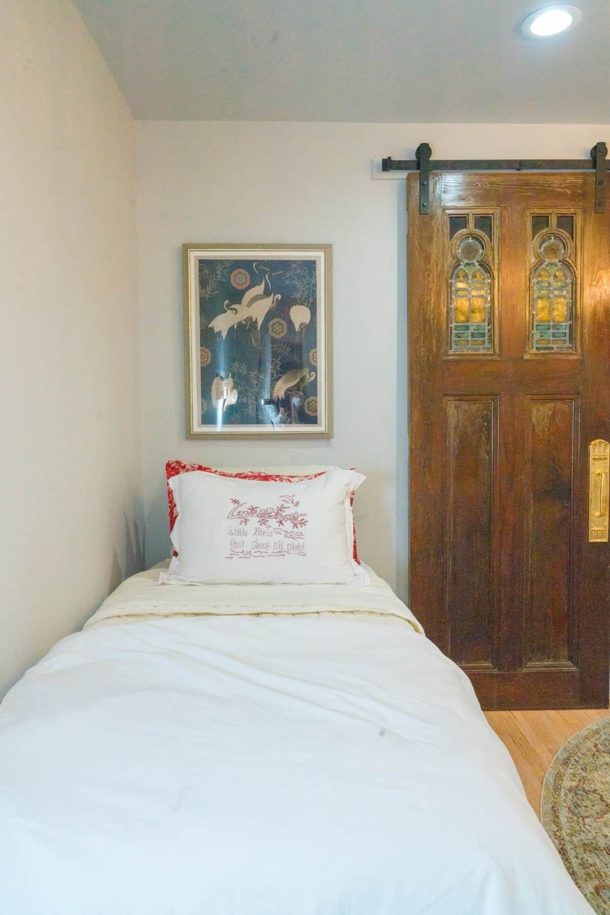 A bedroom with a bed, a wooden door with glass panels, and a framed picture on the wall.