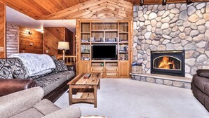 L’intérieur chaleureux d’un chalet en bois, avec une cheminée en pierre, des étagères en bois et un coin salon confortable.