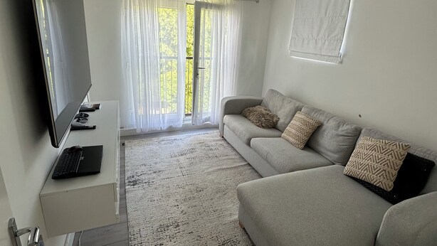 A modern living room with a grey sofa, a flat-screen TV, and a laptop on a white console. - Antonio’s house. One bedroom apartment in London. 8-10mins walk to the station  (London)