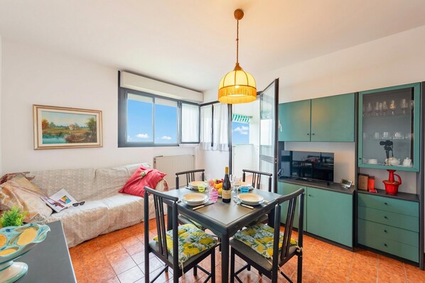 Un coin repas avec une table dressée pour quatre personnes, un canapé, une cuisine équipée d’armoires et une fenêtre offrant une belle vue.
