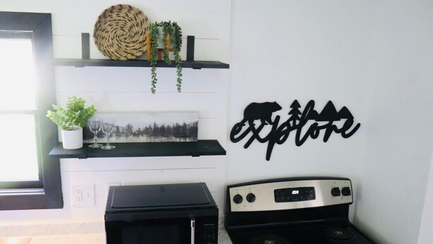 Una cocina con microondas, estufa, repisas con objetos decorativos y un letrero en la pared que dice 'explore'.