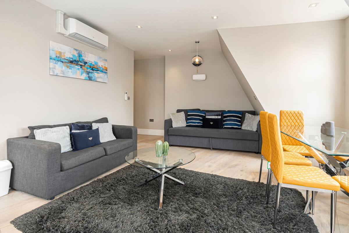 Un appartement moderne avec un canapé gris, une table basse en verre et un coin repas avec des chaises jaunes.