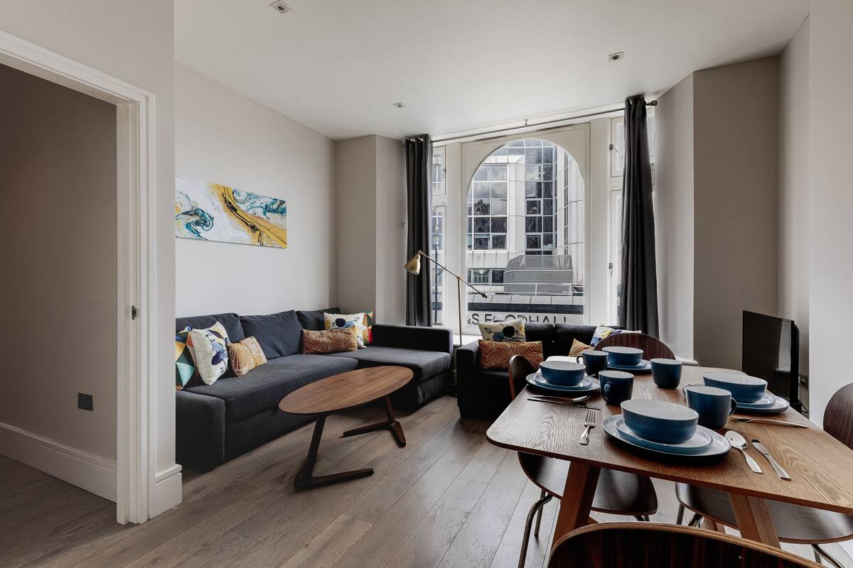 Un salon moderne avec un canapé gris foncé, une table basse en bois et une table à manger agrémentée d’assiettes et de bols bleus.
