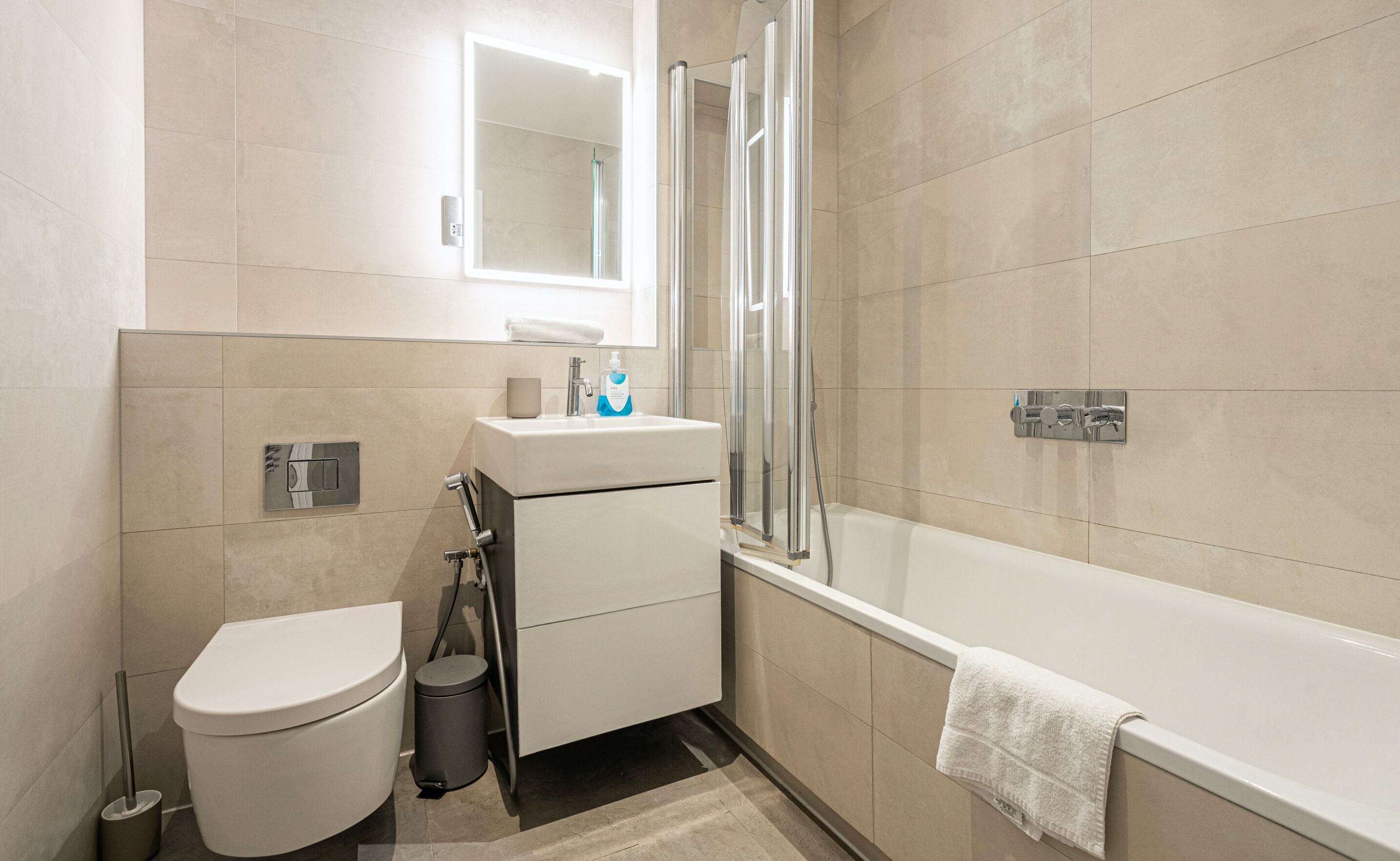 Et moderne badeværelse med toilet, vask, bruser og badekar.