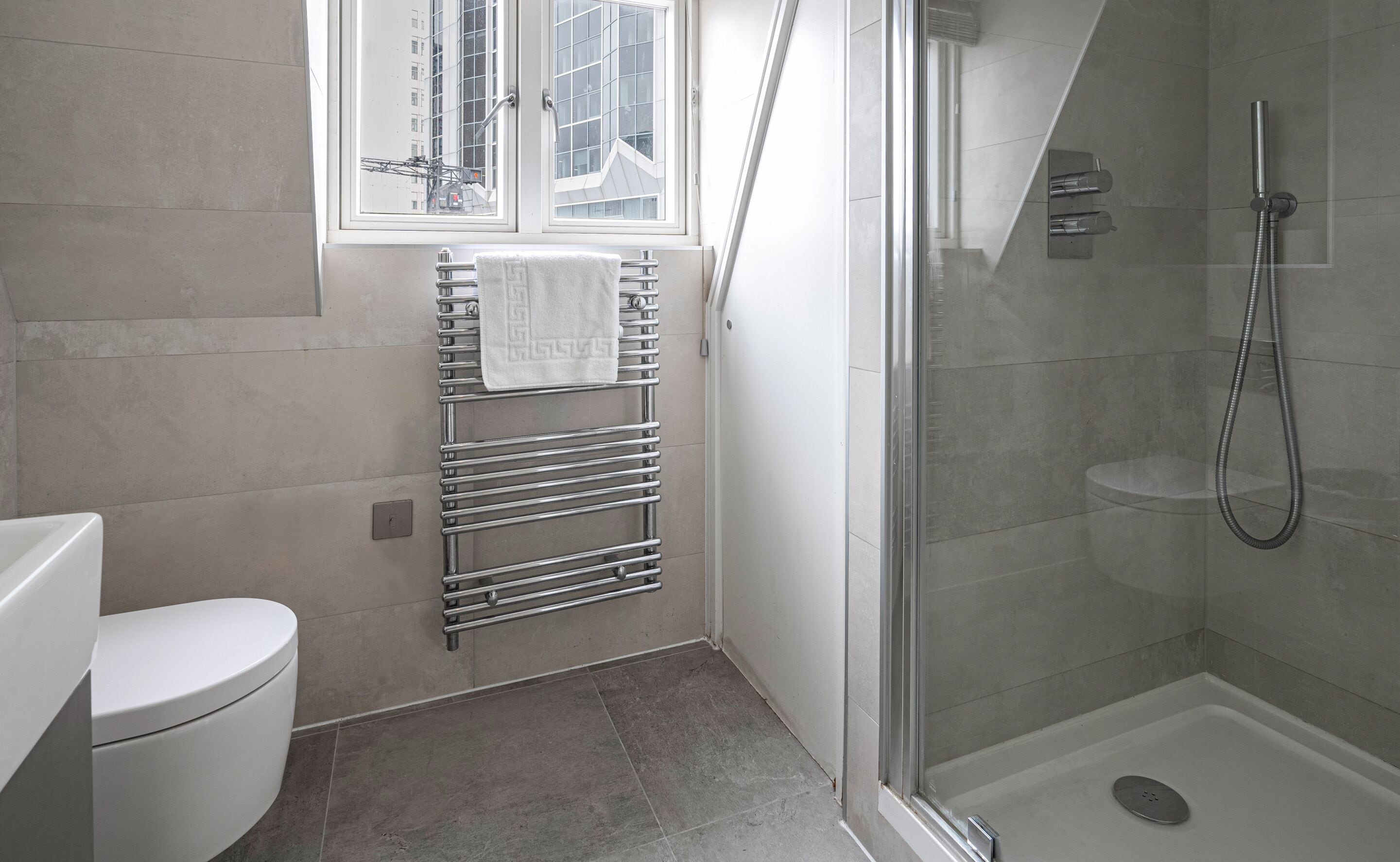 Une salle de bain moderne équipée de toilettes, d’un porte-serviettes et d’une douche séparée par des parois en verre.