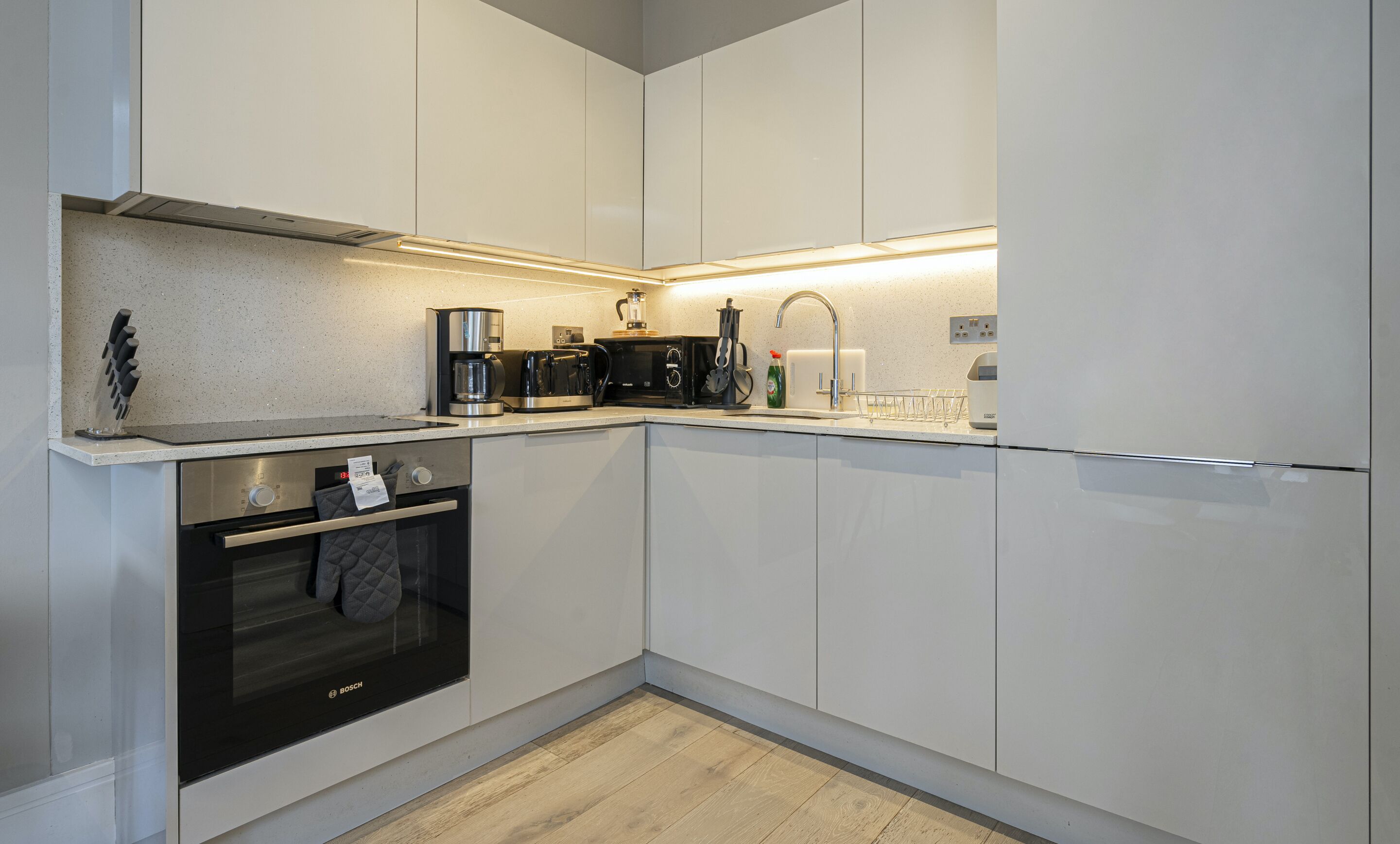 Une cuisine moderne avec des meubles blancs, un four Bosch, une machine à café et un four à micro-ondes.