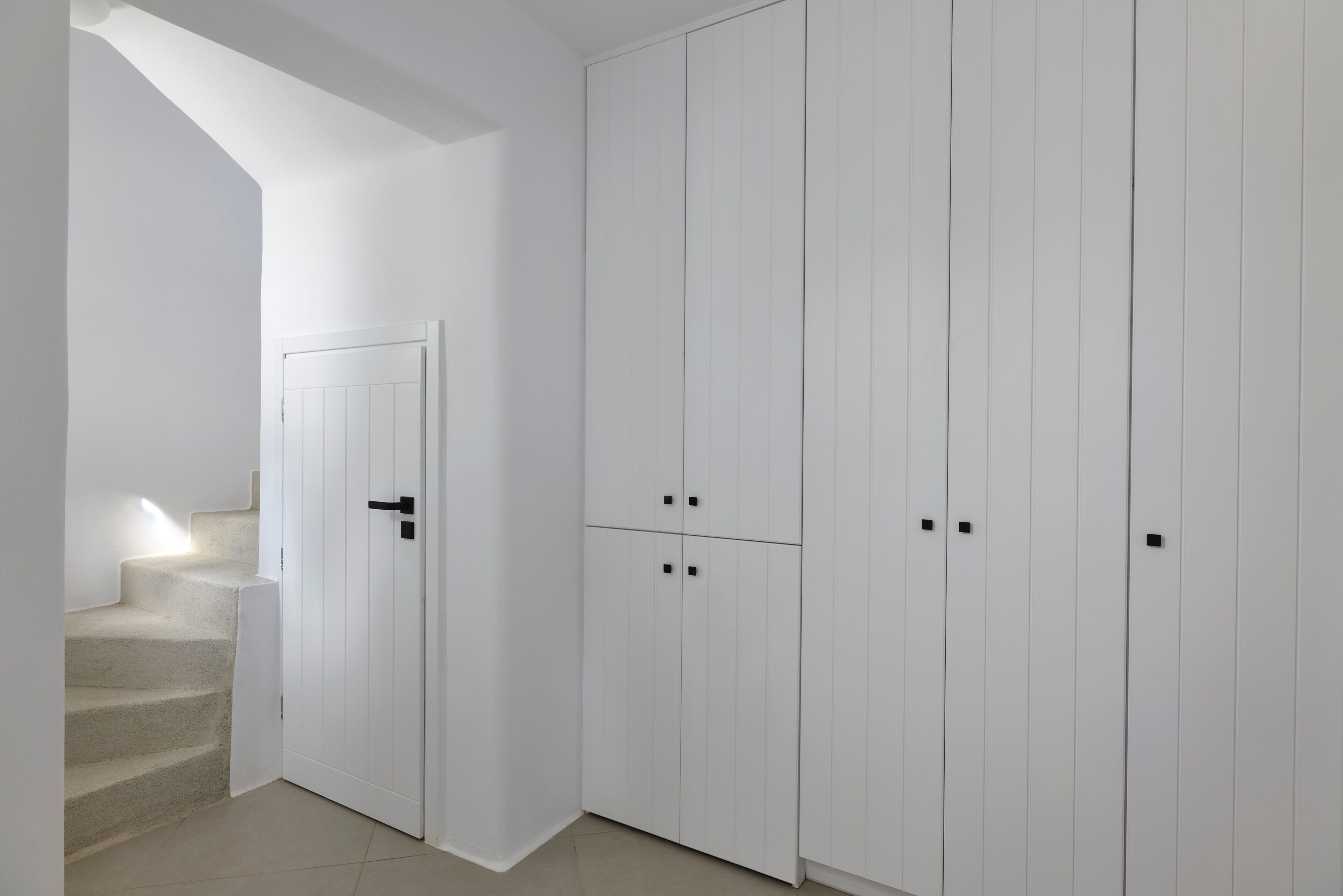 A white interior with a staircase, a door, and a wardrobe with multiple compartments.